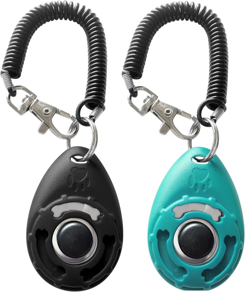Three ergonomic pear-shaped dog training clickers in black and teal, with coiled wrist straps, on a light gray background.